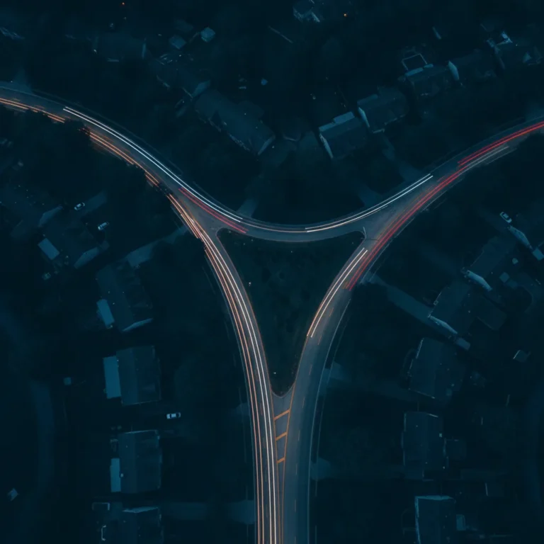 Aerial dusk view of two roads merging with streams of car lights through suburbs